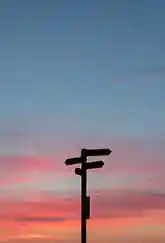 Silhouette of a multi-directional signpost against a pink and orange sunset sky